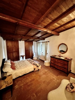Letto elegante con cuscini rosa, tende leggere e arredamento vintage in una stanza toscana.