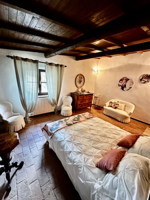 Camera rustica con soffitto in legno, letto matrimoniale, mobili antichi e tonalità calde.