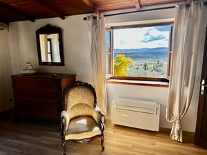 Sedia imbottita accanto a una finestra aperta che incornicia un panorama mozzafiato sulle colline toscane.