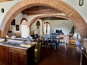 Spazio open space con cucina rustica, sala da pranzo e soggiorno, uniti da suggestivi archi in mattoni rossi.
