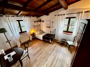 Camera singola con letto in ferro battuto, scrivania antica e tende bianche leggere, in stile country chic.