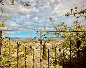 Dettaglio romantico di una ringhiera in ferro battuto decorata con rampicanti, con vista sulle colline toscane.